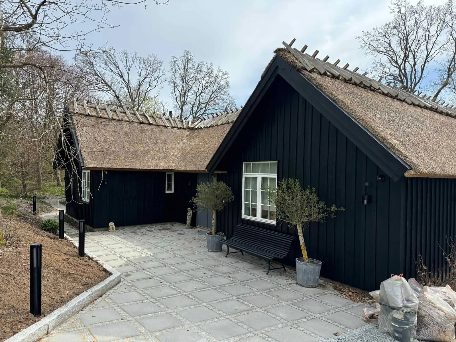 Sortmalet sommerhus med stråtag og nylagt flisebelægning